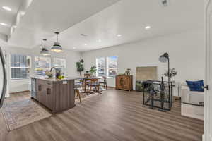Kitchen with light stone counters, decorative light fixtures, a breakfast bar area, dark wood-style flooring, and a center island with sink