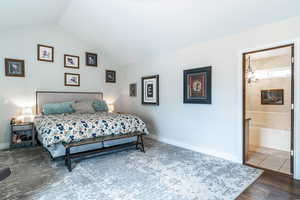 Primary bedroom featuring vaulted ceiling, ensuite bath, and dark wood-style floors