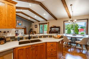 Kitchen featuring brown cabinets, a peninsula, dark wood-style flooring, stainless steel dishwasher, and hanging light fixtures