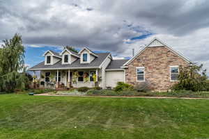 New england style home with covered porch, a front yard, roof with shingles, and stone siding