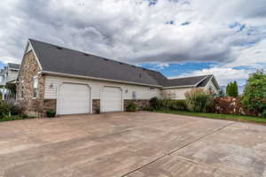 View of property exterior with stone siding, driveway, and a shingled roof