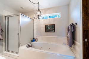 Primary bath featuring a stall shower, a whirlpool tub, and a chandelier