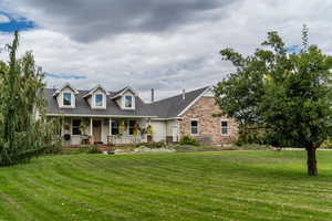 New england style home with a porch, a front yard, stone siding, and roof with shingles