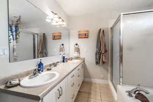 Primary full bath with light tile patterned floors, a stall shower, double vanity, and a bath