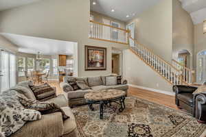 Living area with high vaulted ceiling, healthy amount of natural light, a chandelier, stairs, and light wood-type flooring