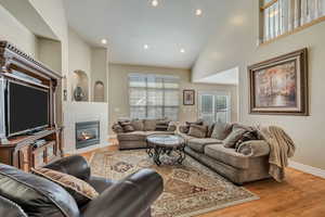 Living area featuring light wood-style floors, a tiled fireplace, recessed lighting, and high vaulted ceiling