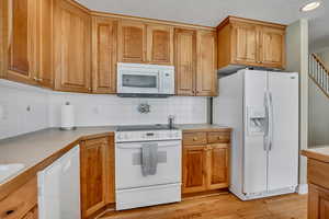 Kitchen featuring white appliances, tasteful backsplash, light countertops, light wood finished floors, and recessed lighting