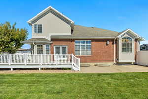 Back of property with a yard, a deck, a shingled roof, and brick siding