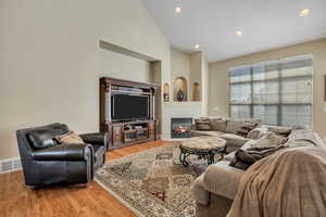 Living room with light wood-style flooring, a tile fireplace, recessed lighting, and high vaulted ceiling