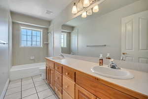 Bathroom with double vanity, shower / bath combination, and light tile patterned flooring