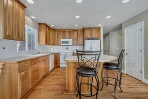 Kitchen featuring light countertops, a breakfast bar area, white appliances, light wood finished floors, and recessed lighting