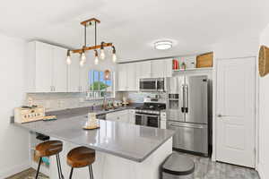 Kitchen with a peninsula, appliances with stainless steel finishes, white cabinets, a breakfast bar, and backsplash