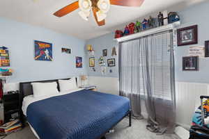 Bedroom featuring carpet, a ceiling fan, and wainscoting