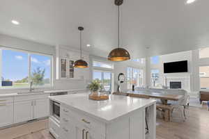 Kitchen featuring white cabinets, recessed lighting, a fireplace, light wood finished floors, and pendant lighting