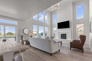 Living room with light wood finished floors, a glass covered fireplace, a towering ceiling, and a chandelier