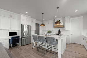 Kitchen with backsplash, appliances with stainless steel finishes, white cabinetry, hanging light fixtures, and a breakfast bar area