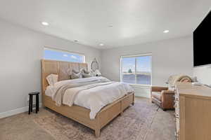 Primary bedroom with multiple windows, light colored carpet, and recessed lighting