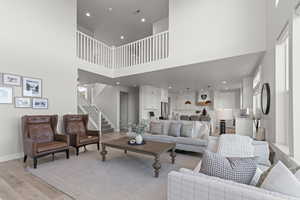 Living room with a high ceiling, light wood-type flooring, recessed lighting, and stairs