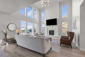 Living area featuring a high ceiling, light wood finished floors, a glass covered fireplace, healthy amount of natural light, and a chandelier