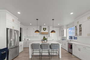 Kitchen featuring stainless steel appliances, a breakfast bar, white cabinetry, hanging light fixtures, and a kitchen island