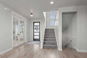 Entrance foyer with healthy amount of natural light, stairway, light wood finished floors, french doors, and recessed lighting