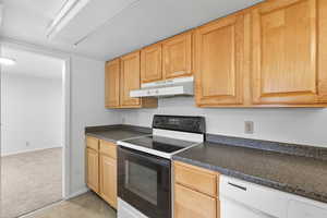Kitchen featuring black range with electric cooktop, light carpet, dark countertops, under cabinet range hood, and light brown cabinetry