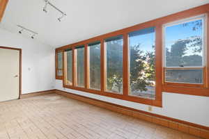 Unfurnished sunroom with track lighting and lofted ceiling