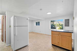 Kitchen with freestanding refrigerator, electric panel, and dark countertops