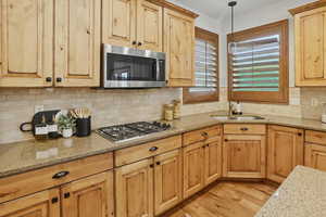 Kitchen with light stone countertops, hanging light fixtures, light wood finished floors, and decorative backsplash