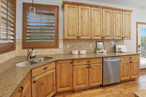 Kitchen with light stone counters, stainless steel dishwasher, decorative light fixtures, and backsplash