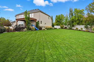 Rear view of house with a fenced backyard, stucco siding, stairs, and stone siding