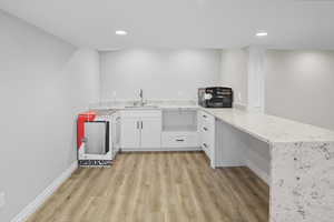 Kitchen featuring a peninsula, light stone countertops, white cabinetry, light wood-style floors, and recessed lighting
