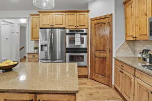 Kitchen with stainless steel appliances, light wood-style flooring, light stone countertops, tasteful backsplash, and light brown cabinets