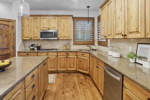 Kitchen with light wood-style flooring, stainless steel appliances, light stone countertops, and pendant lighting