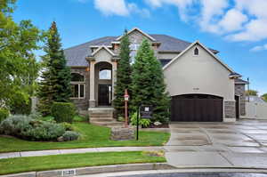 View of front of property featuring stone siding, stucco siding, concrete driveway, and roof with shingles