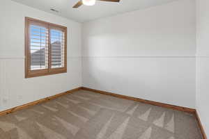 Empty room with a wainscoted wall, a ceiling fan, and carpet