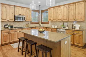 Kitchen with decorative light fixtures, light stone countertops, light wood-style flooring, and appliances with stainless steel finishes