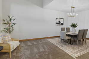 Carpeted dining area with baseboards and a chandelier
