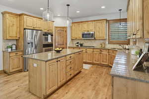 Kitchen with light stone countertops, decorative backsplash, hanging light fixtures, stainless steel appliances, and light wood-style floors