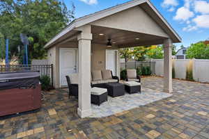 Fenced backyard with ceiling fan, a patio, a hot tub, and an outdoor living space