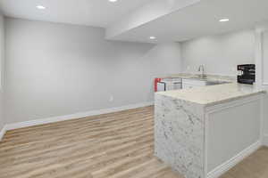 Kitchen with a peninsula, light stone countertops, recessed lighting, light wood-style flooring, and white cabinetry