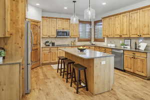 Kitchen featuring light stone countertops, pendant lighting, light wood-style floors, a kitchen breakfast bar, and a center island