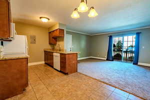 Kitchen featuring light colored carpet, brown cabinets, hanging light fixtures, light tile patterned floors, and light stone counters
