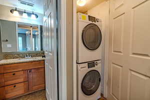 Washroom with stacked washing machine and dryer, dark tile patterned floors, a textured ceiling, and a textured wall