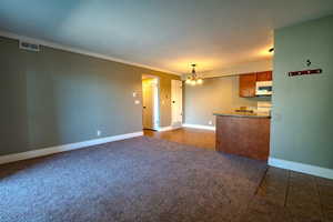 Unfurnished living room featuring a chandelier, dark colored carpet, dark tile patterned floors, ornamental molding, and a textured ceiling