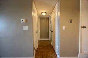 Hallway featuring a textured wall and dark tile patterned flooring
