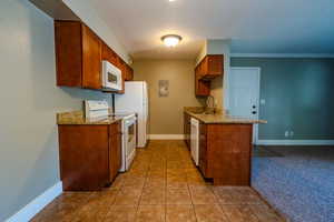 Kitchen featuring light stone countertops, white appliances, light tile patterned floors, brown cabinetry, and a textured ceiling