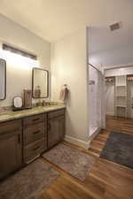 Bathroom with a stall shower, double vanity, light wood-style flooring, and a walk in closet