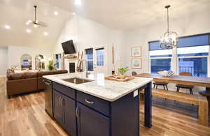 Kitchen with light stone countertops, light wood finished floors, high vaulted ceiling, decorative light fixtures, and a fireplace