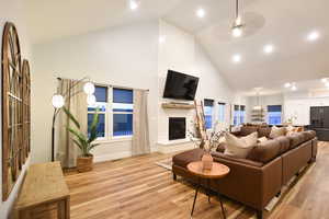Living area featuring high vaulted ceiling, light wood finished floors, a large fireplace, ceiling fan, and recessed lighting
